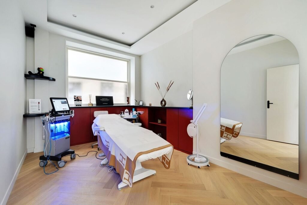 配备 HydraFacial 仪器的美容诊疗室，房间内有白色护理床、蓝光医美设备推车、工作台及落地镜，环境整洁明亮