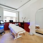 配备 HydraFacial 仪器的美容诊疗室，房间内有白色护理床、蓝光医美设备推车、工作台及落地镜，环境整洁明亮